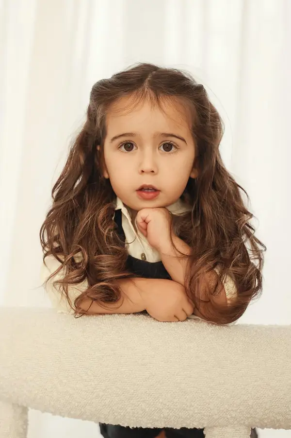 Girl with long curly hair resting her chin on a cream chair, studio photography by Photoholic, Monsey NY