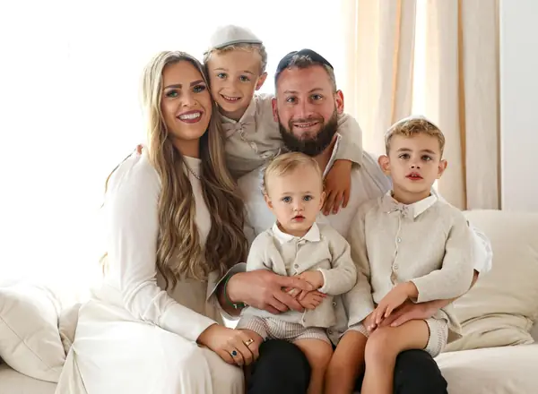 Family of five cuddled together on a white sofa, studio photography by Photoholic, Monsey NY
